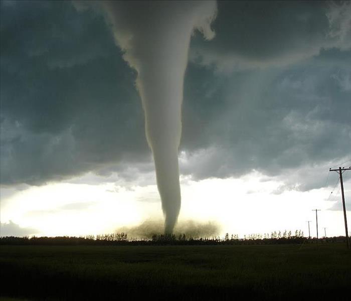 Large grey clouds with a tornado touching down in an open field.