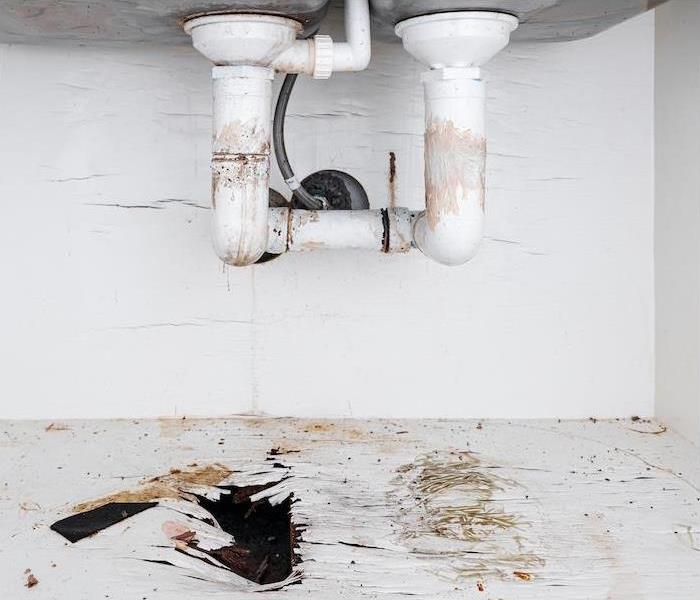 "the underside of a sink showing water damage from leaking pipes”
