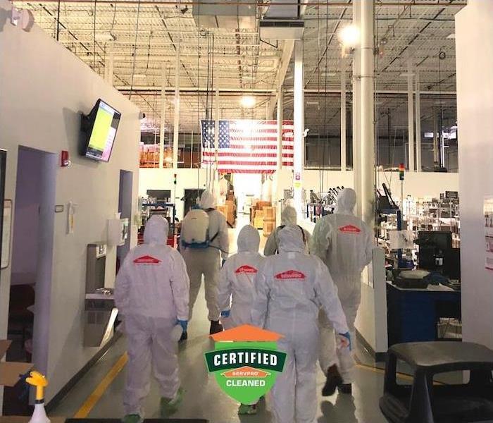 A crew of SERVPRO employees in PPE gear walking inside commercial building.
